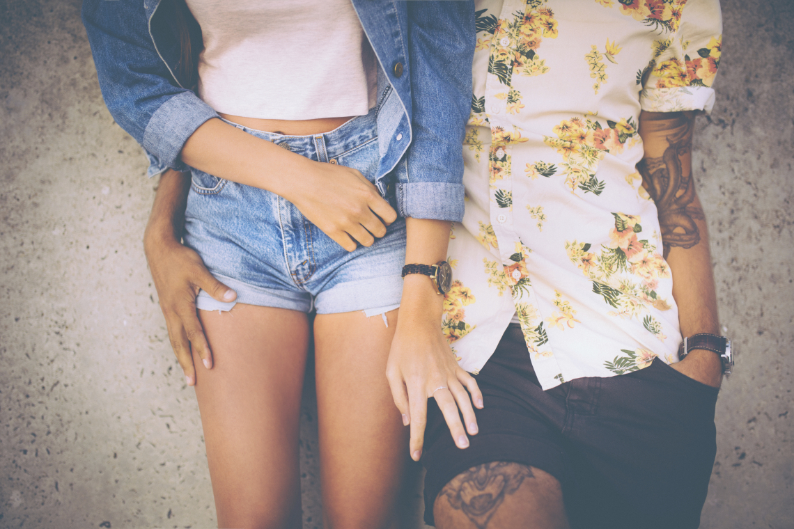 Cropped midsection of a hipster couple standing close together and leaning against a wall in retro style clothing