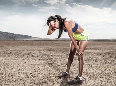 A women athlete bent over in an arid desert envirnoment.