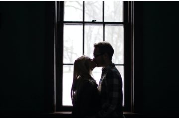 Žena a muž sa bozkávajú pri okne