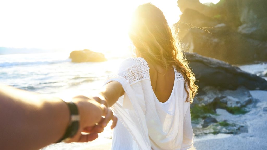 Muž drží ženu za ruku pri západe slnka