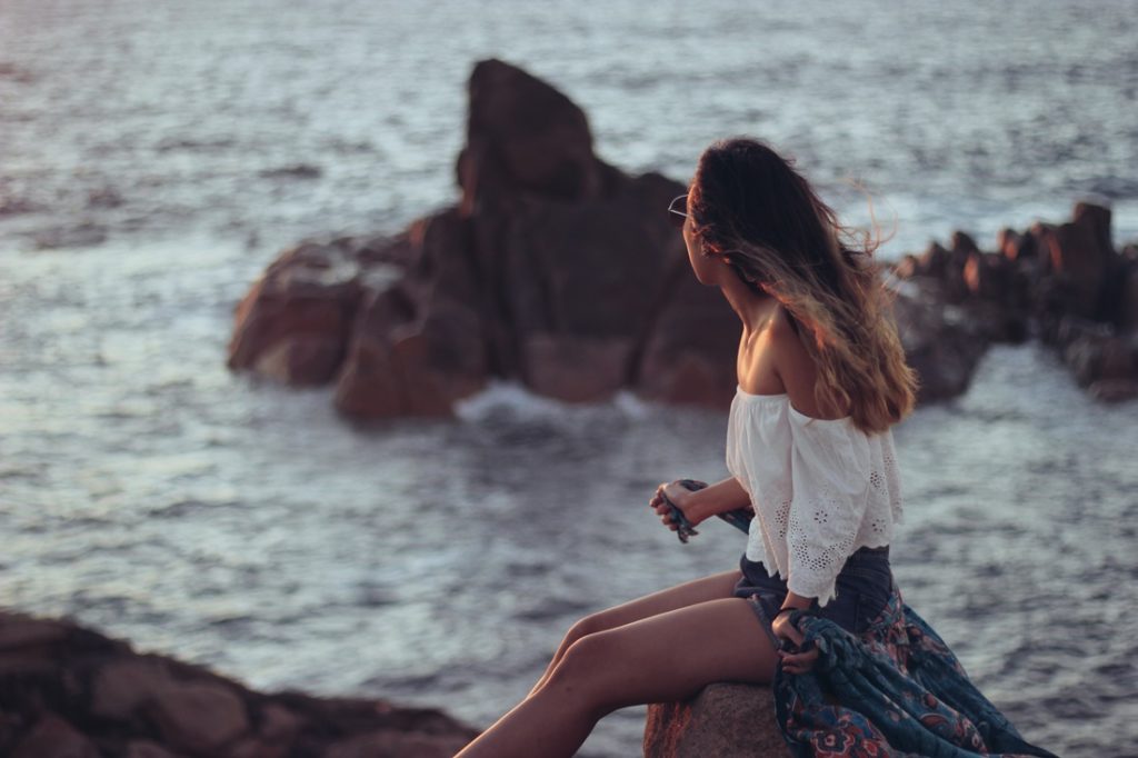 Žena pri mori sedí na skale