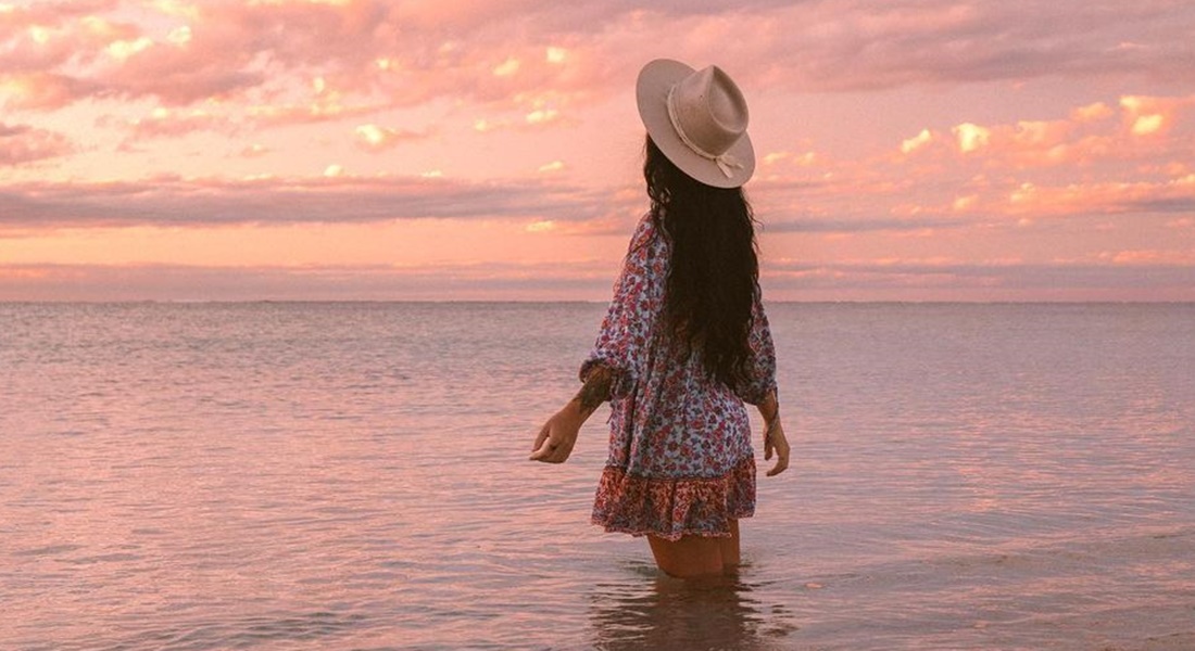 Žena stojí v mori pri západe slnka