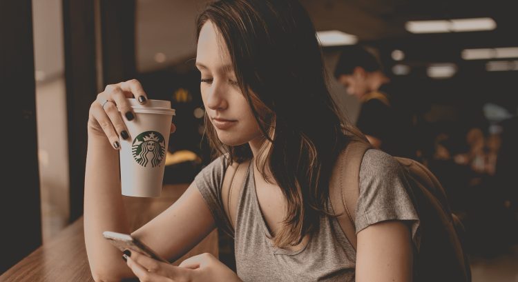 Mladá žena sedí v kaviarni s mobilom