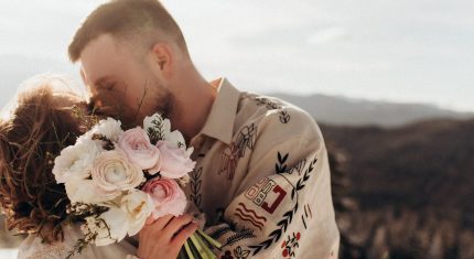 Žena drží kyticu kvetov a bozkáva muža