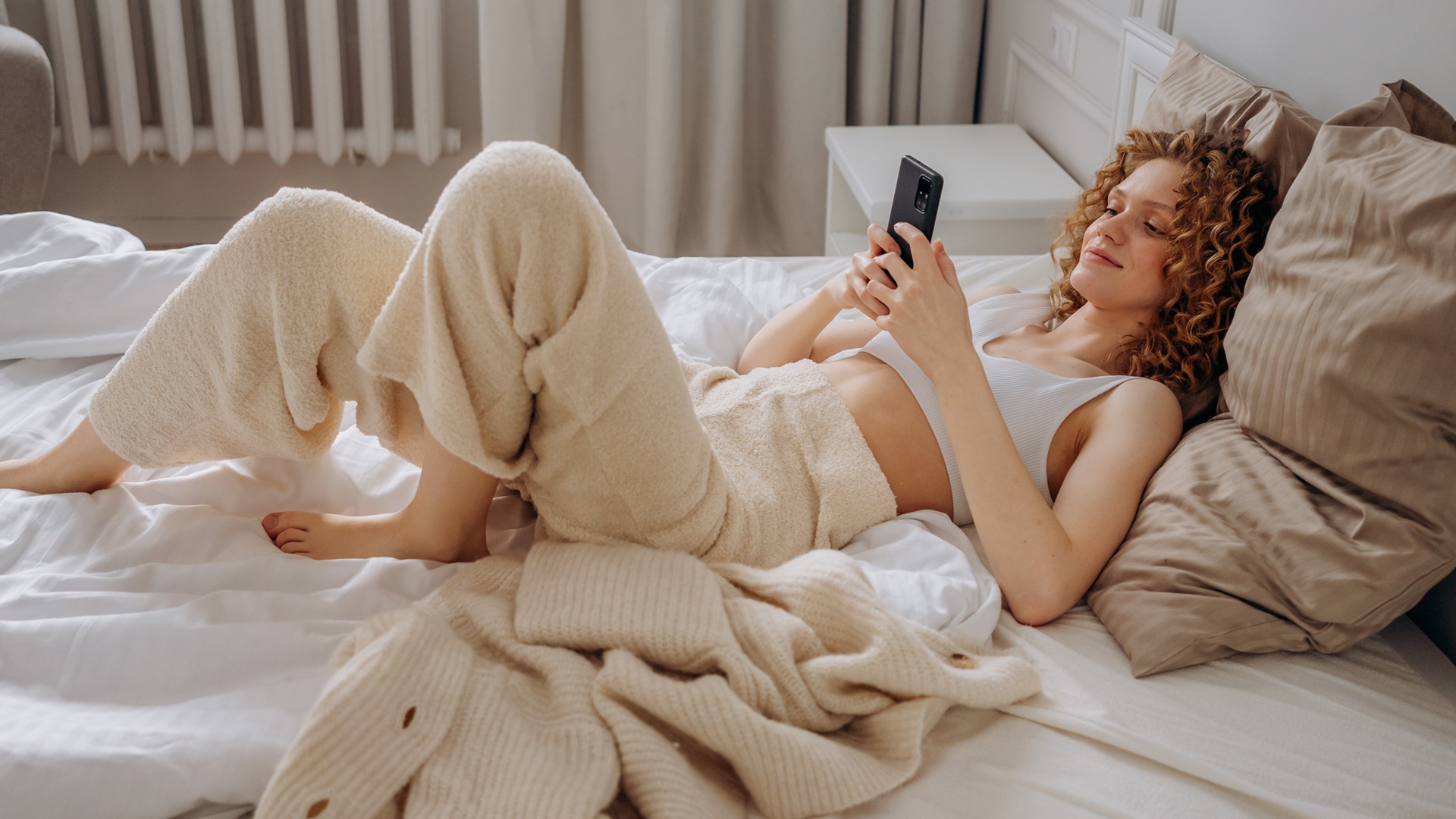 Žena leží v posteli a hrá sa na mobile
