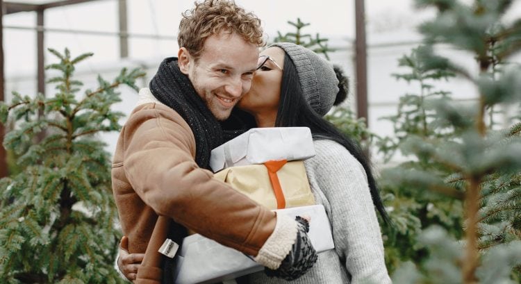 Muž drží darčeky a žena ho bozkáva na líce