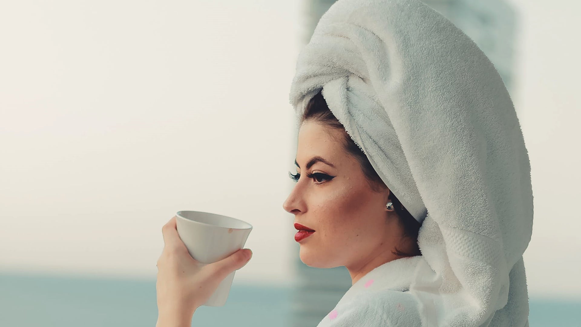 Žena s uterákom na hlave pije ráno kávu
